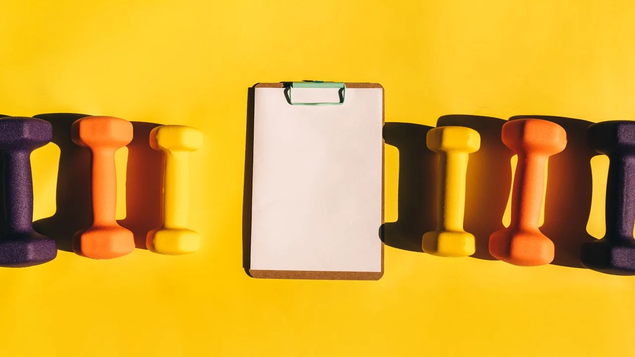 Coloured dumbbells around a blank clipboard on yellow