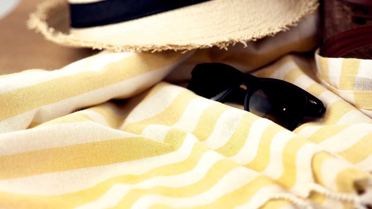 A sun hat and sunglasses beside a striped towel