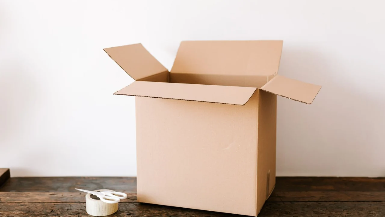 An open unmarked cardboard box with packing tape and scissors on a wooden table