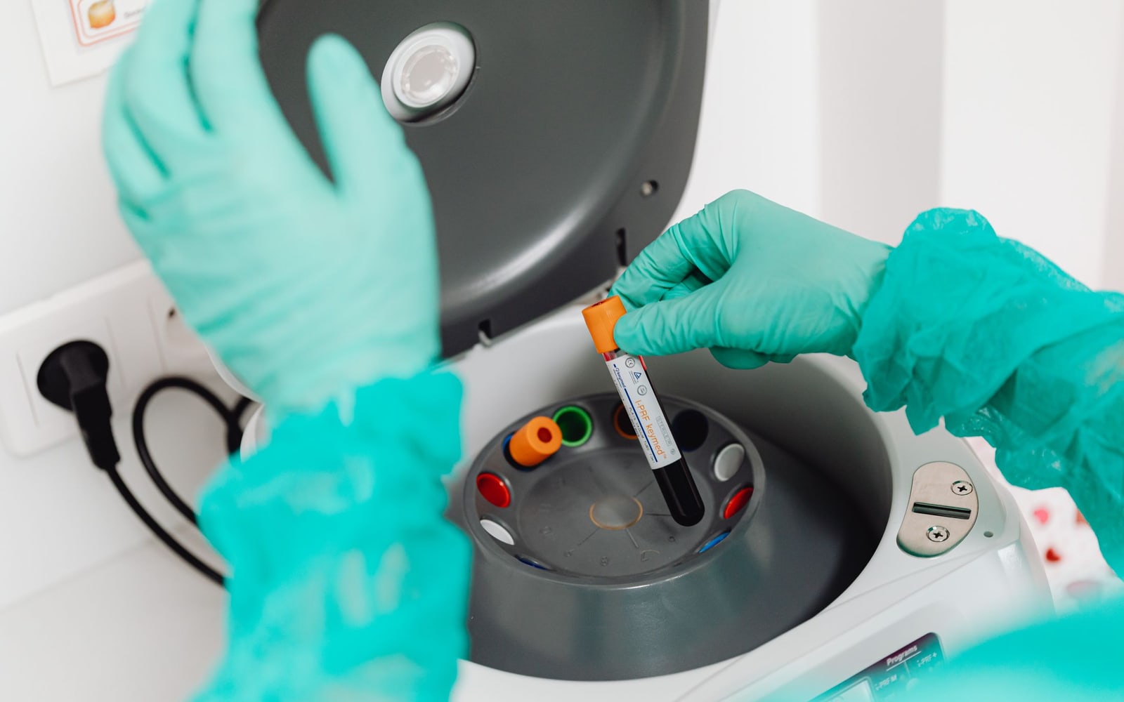 A lab technician wearing gloves uses a centrifuge for blood analysis in a modern laboratory setting.