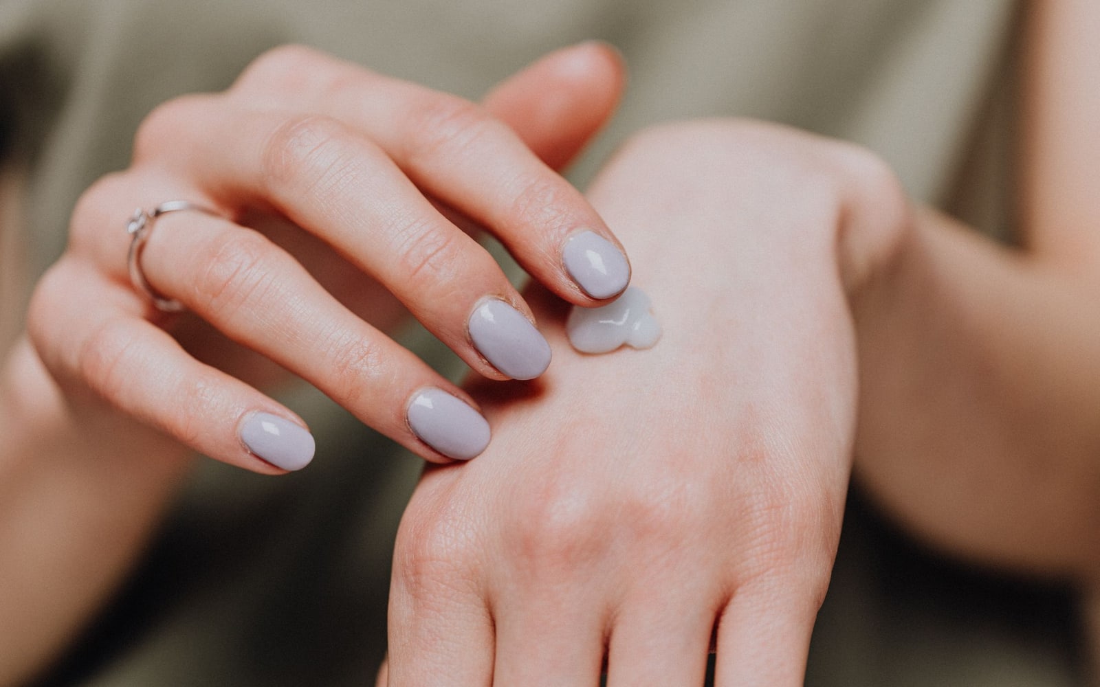 A hand applying a small amount of cream to the other hand.