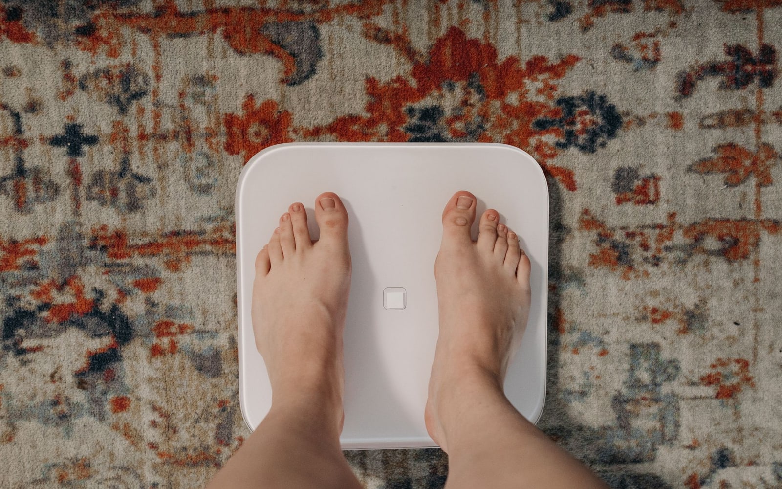 Bare feet on a white digital bathroom scale over a patterned rug.